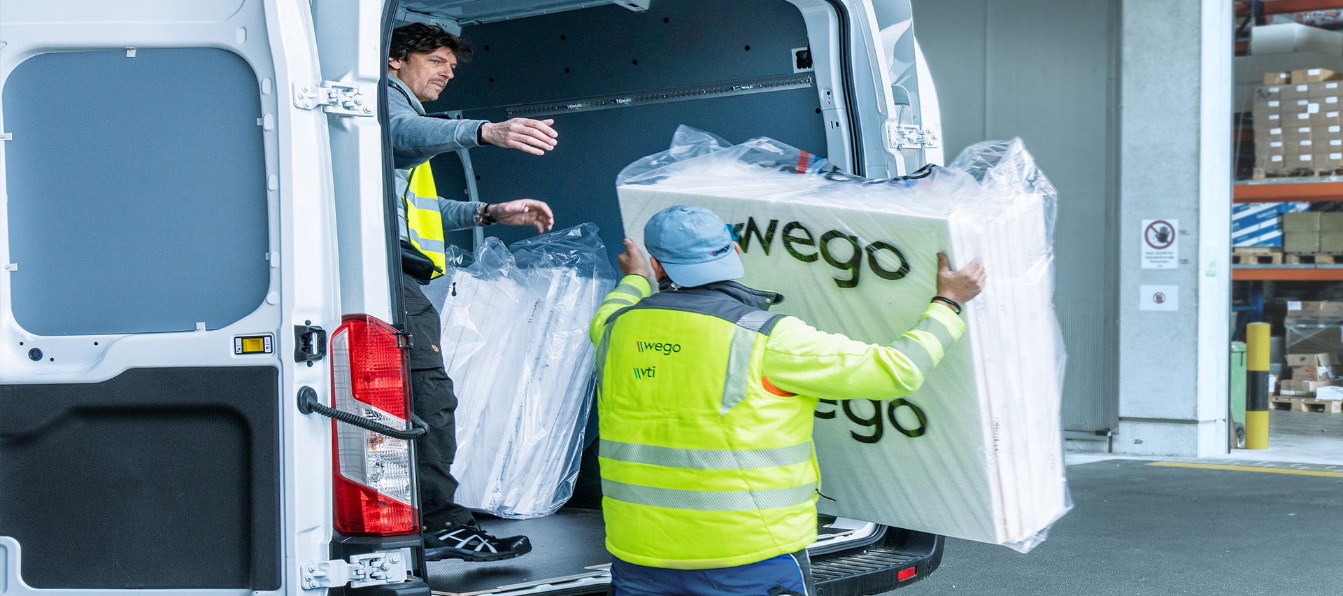 Zwei Mitarbeiter laden Baustoffe in den Lieferwagen bei Wego Systembaustoffe.